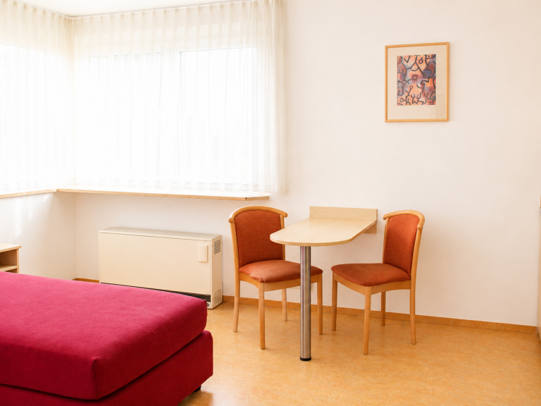 Ein Zimmer mit einem roten Sofa, einem Tisch und zwei Stühlen vor einem Fenster.