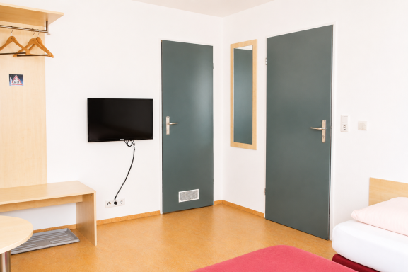 Helle Hotelzimmer mit einem Bett, Fernseher, Tisch und zwei Türen.