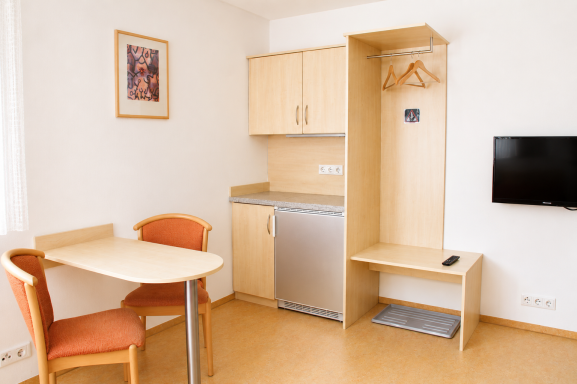Kleine Wohnung mit Tisch, Stühlen, Küchenzeile und TV in neutralem Design.