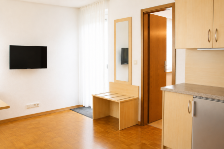 Helle, moderne Wohnung mit Fernseher, Tisch und Sicht auf die Tür.