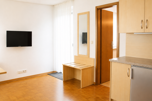 Helle, moderne Wohnung mit Fernseher, Tisch und Stuhl sowie Küchenbereich.