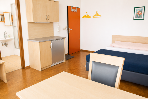 Heller Hotelzimmer mit einem Bett, Tisch, Kühlschrank und Badezimmerbereich.