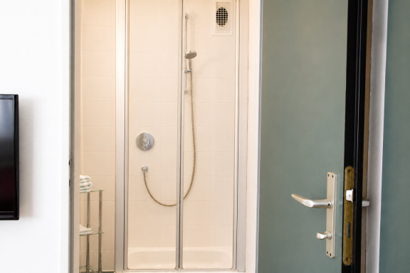 Duschkabine mit Glastür, Wandhahn und Handbrause in einem modernen Badezimmer.