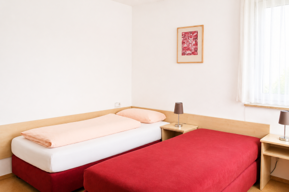 Helles Zimmer mit einem Einzel- und einem Doppelbett sowie Nachttischen.