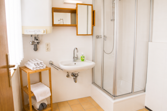 Helles Badezimmer mit Dusche, Waschbecken und Holzregal.